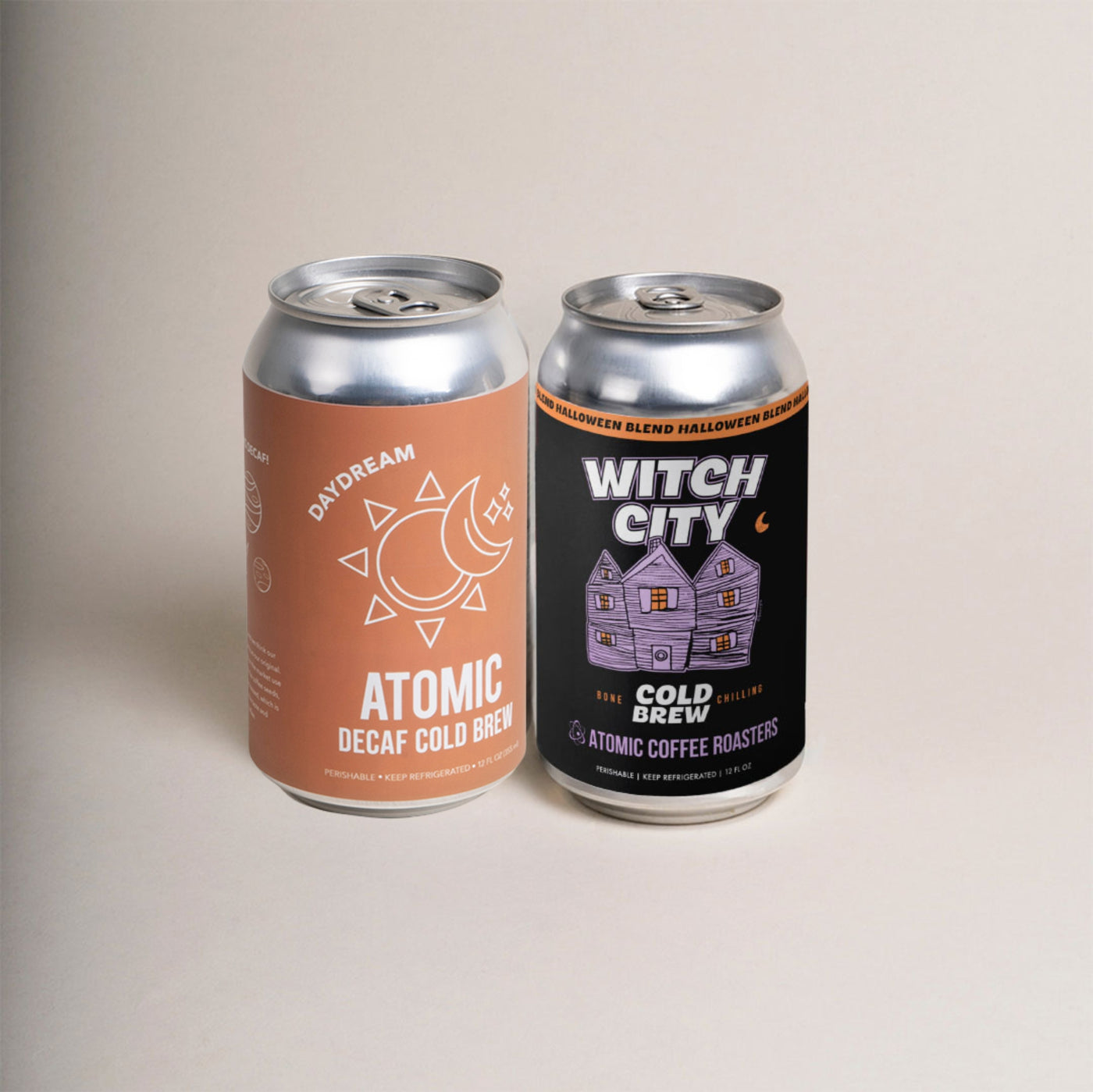 Two 12 oz cans, one orange can that says "Atomic Daydream Decaf Cold Brew" and one black can that says "Witch City Cold Brew" with Halloween artwork.