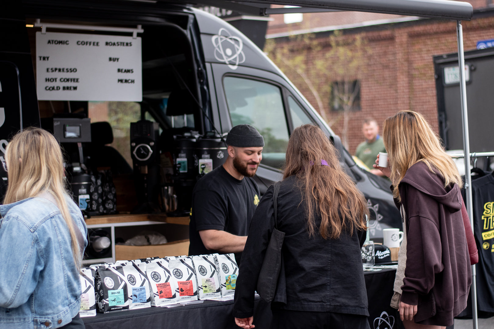 Coffee truck with customers and a menu board, set against a brick building.